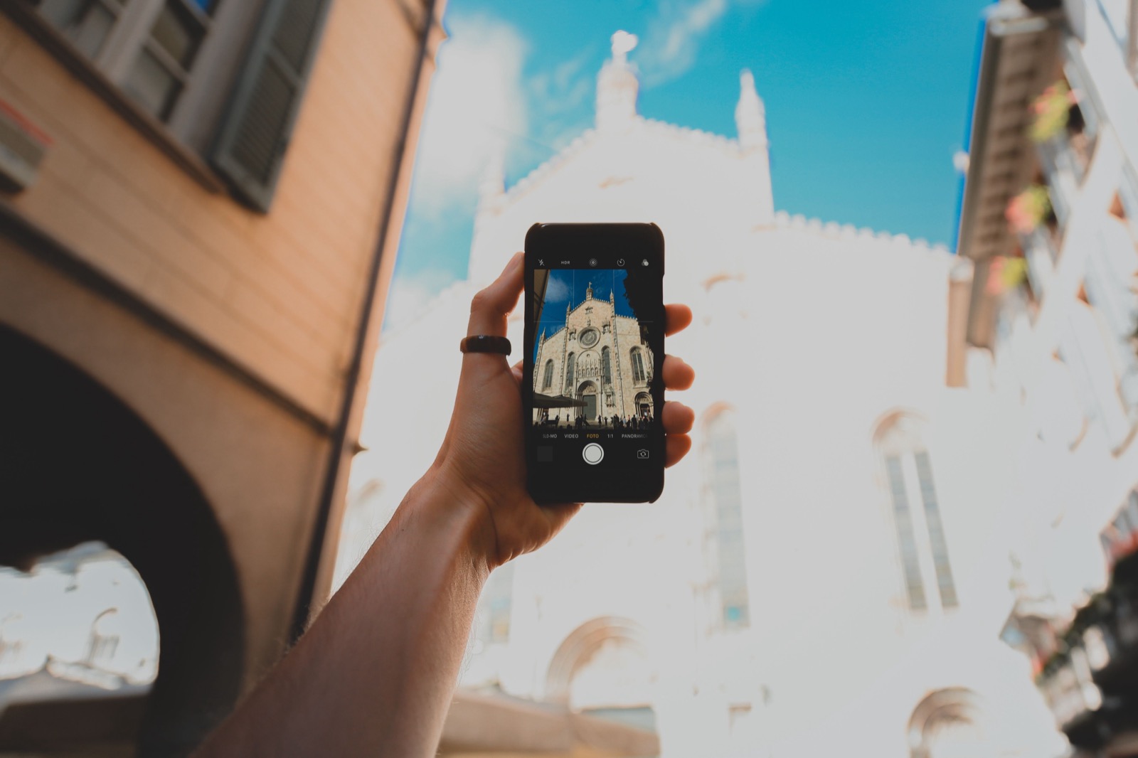 A hand holding up a phone to film a sunlit cathedral facade on an Italian street.